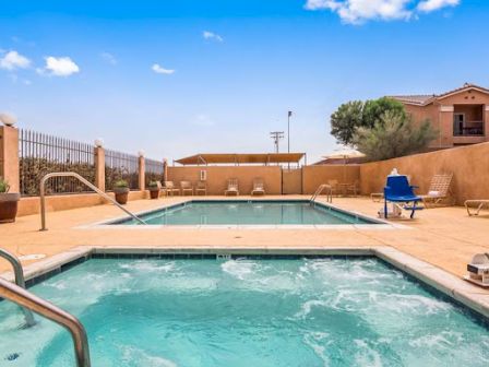 The image shows an outdoor pool area with a swimming pool, a hot tub, lounge chairs, and pool lifts under a clear blue sky.