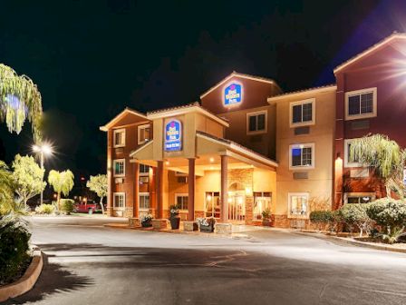 The image shows the exterior of a Best Western Plus hotel at night, with bright lights illuminating the entrance and surrounding palm trees.