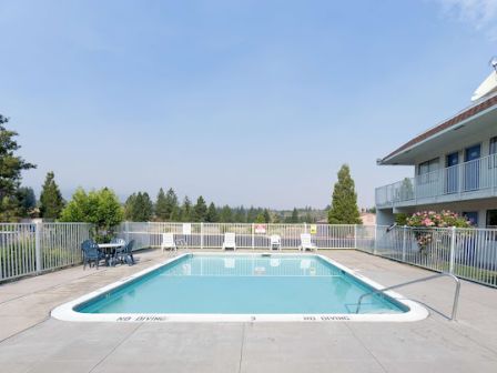 A fenced outdoor pool at a hotel with surrounding chairs, tables, and a building nearby under a clear sky.