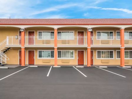 The image shows a two-story motel with multiple rooms, exterior staircases, and an empty parking lot in front.