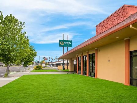 A street view with a grassy lawn, trees, and a building with a sloped roof; a 