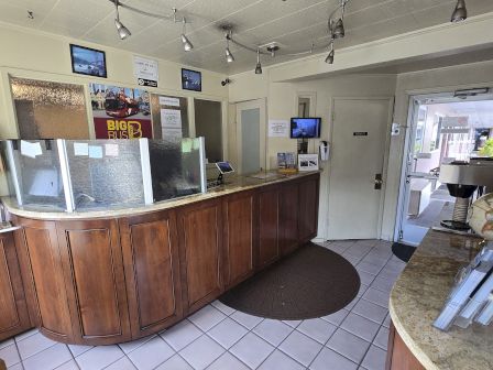 The image shows a motel reception area with a curved wooden desk, brochures, a globe, and photos on the walls.