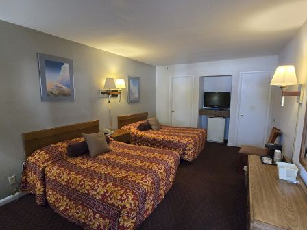 A hotel room with two double beds, patterned bedspreads, wall lamps, a TV, and a dresser with a mirror and essentials.