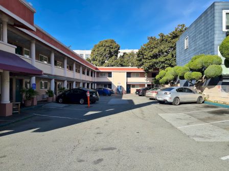 The image shows a parking area of a motel or inn with parked cars, a two-story building, and trees in the background.