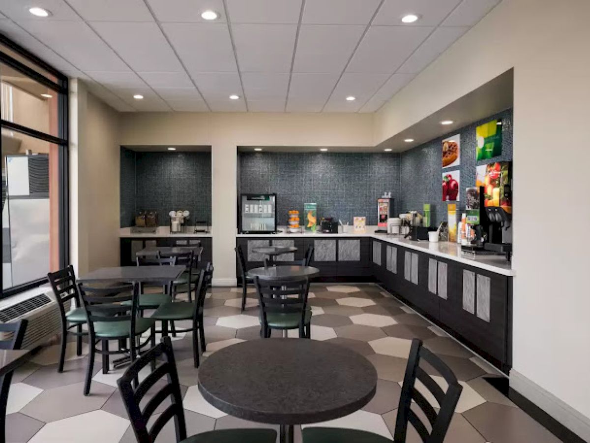 The image shows a modern café with round tables and chairs, a counter with coffee and drink dispensers in the background, and tiled flooring.