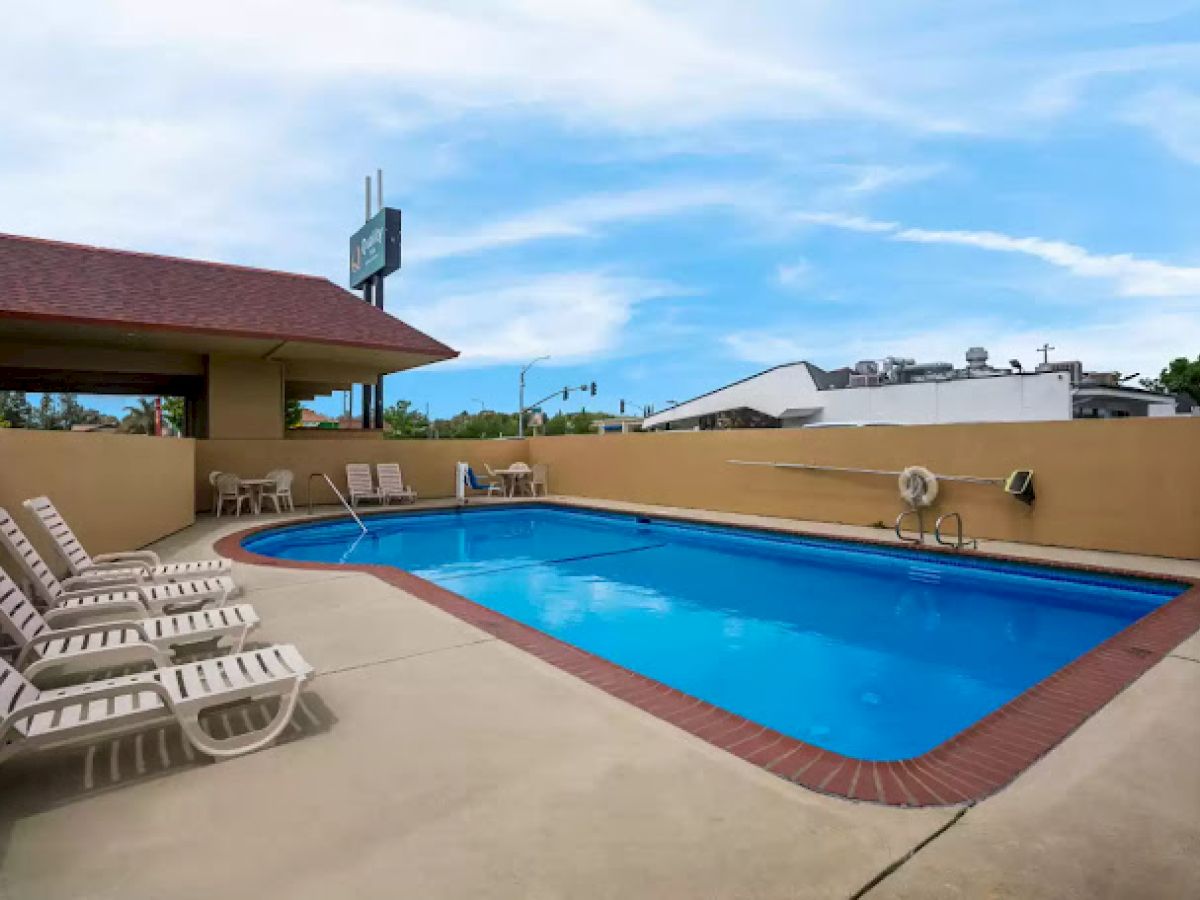 The image shows an outdoor pool with lounge chairs and a building in the background under a blue sky.