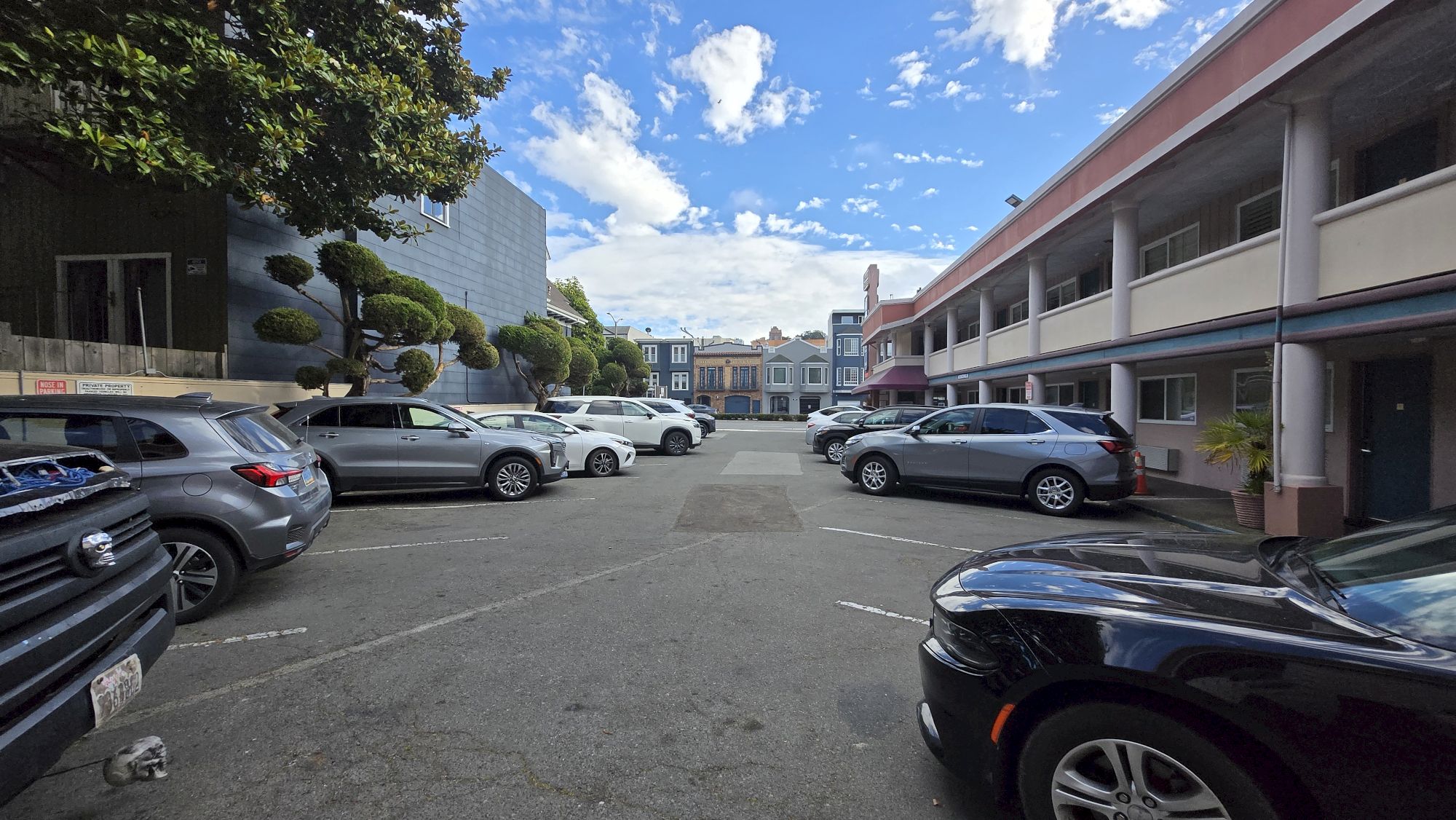 A parking lot with several cars, surrounded by buildings under a partly cloudy sky.