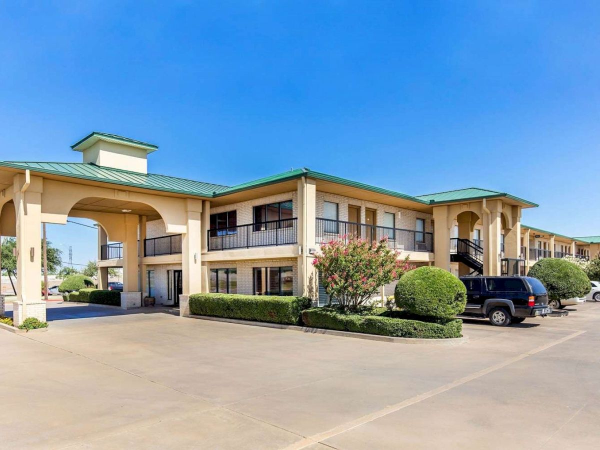 A two-story motel with green roofs, a parking lot, and several cars parked outside on a sunny day.