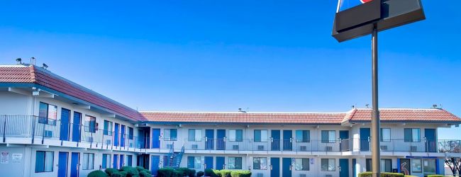 The image shows a Motel 6 building with a large sign, featuring a multi-story layout and a parking area in front.