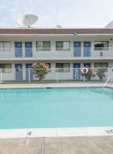 The image shows a hotel pool area with a two-story building, lounge chairs, and a 