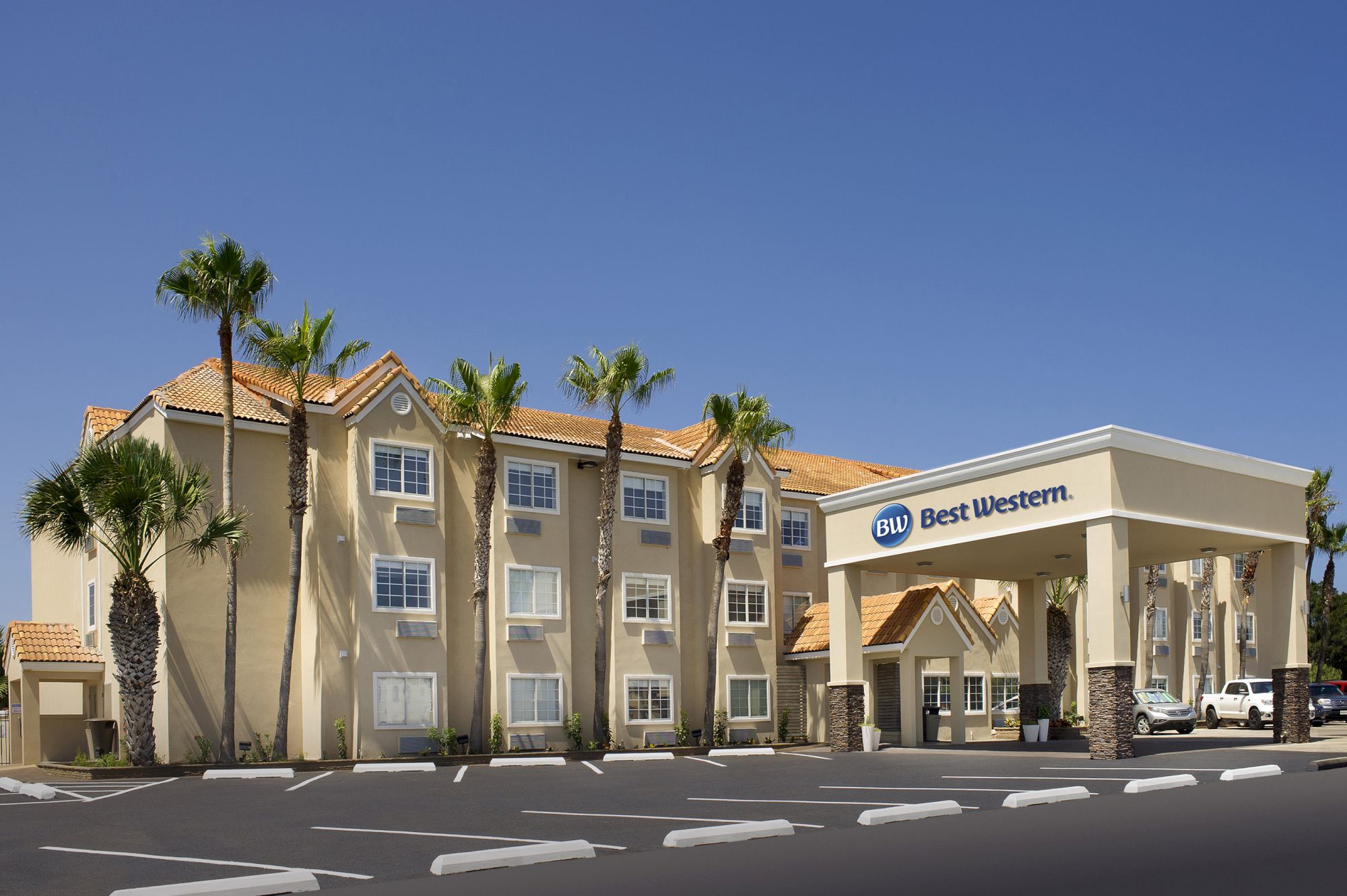 A Best Western hotel with palm trees, featuring a beige building and an entrance canopy in a sunny setting.