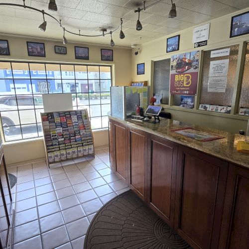 The image shows a reception area with brochures, a counter, coffee machine, and TV screen, featuring large windows and wall decor.