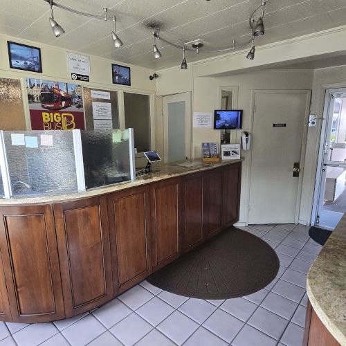 The image shows a reception area with a wooden counter, brochure rack, and a globe. There are various framed photos on the walls.