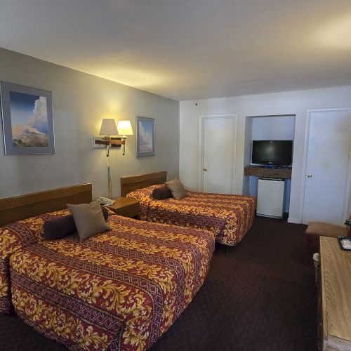 A hotel room with two beds, wall art, lamps, a TV, a dresser, and a mirror. Chairs are also visible along with patterned bedding.