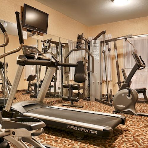 This image shows a fitness room with exercise equipment, including a treadmill, stationary bikes, and weight machines, on a patterned carpet.