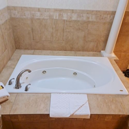 This image shows a bathtub with beige tile surroundings and elegant column accents, complete with folded towels on the side.