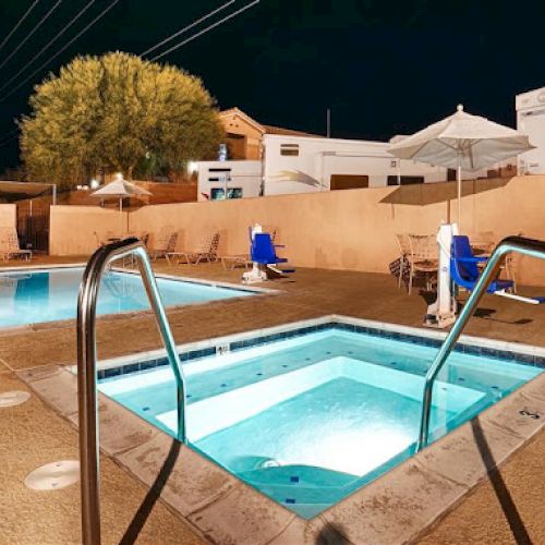 The image shows a night-time view of a swimming pool and a hot tub in an outdoor setting, with lounge chairs and umbrellas nearby.