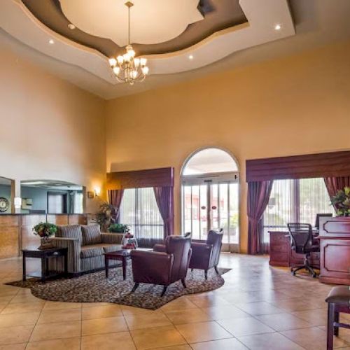 The image shows a spacious hotel lobby with a chandelier, seating area, reception desk, and large windows with curtains.