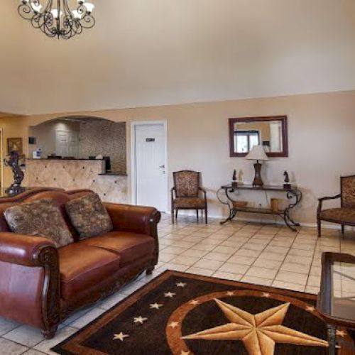 A lobby area with leather sofas, a chandelier, wall art, and a mounted TV. A front desk and decorative table are also visible in the space.