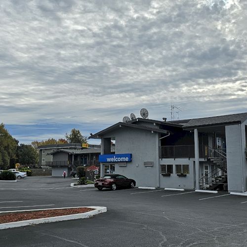 The image shows a Motel 6 building with a parking lot and a prominent sign under a cloudy sky.