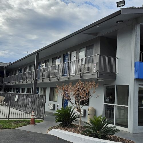 This image shows a two-story motel with a welcome sign, outdoor pool area, and surrounding greenery.