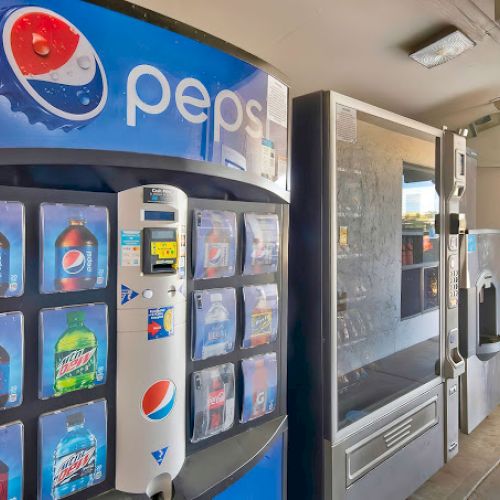 A row of vending machines, one dispensing Pepsi products with various drinks visible on display in a well-lit area.