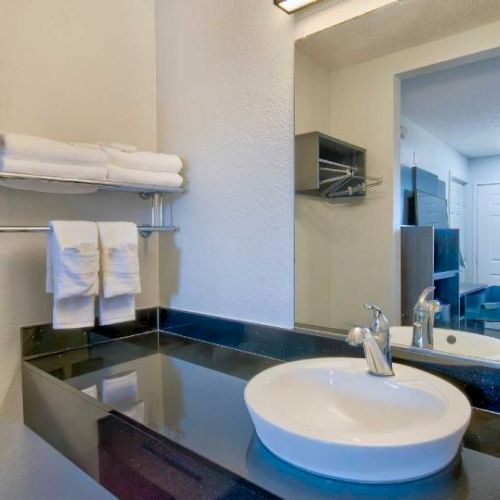 A bathroom with a modern sink, mirror, and towel rack. Towels are neatly arranged on a shelf above the counter.