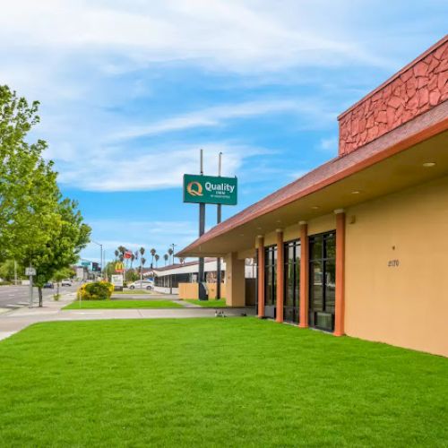 The image shows a commercial building with a lawn, a tree, and a sign for 