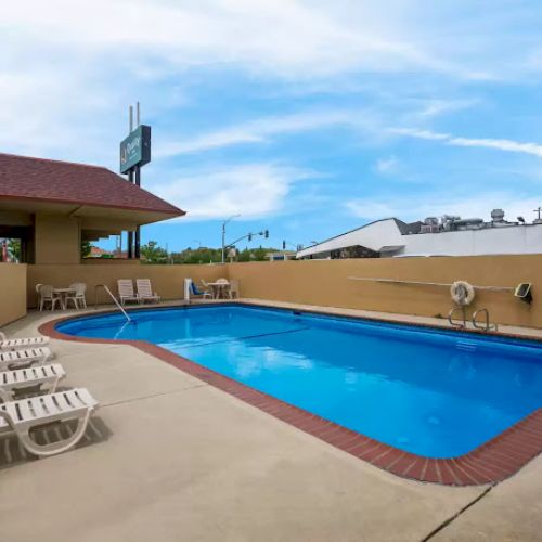 A small outdoor swimming pool with surrounding lounge chairs, a safety ring, and a clear sky backdrop.