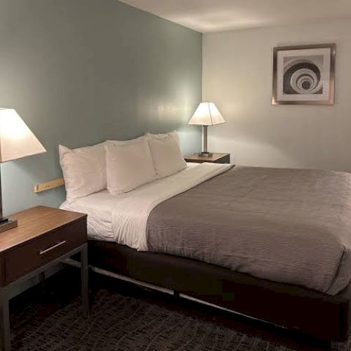 A neatly made bed with gray bedding is flanked by two bedside tables and lamps, in a room with a modern decor and framed wall art.