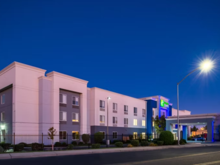 The image shows a modern hotel building at dusk, with exterior lighting and a bright streetlamp illuminating the area.