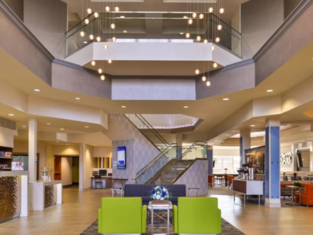 A modern hotel lobby with seating area, bright green chairs, staircase, and contemporary lighting design adorn the spacious interior.