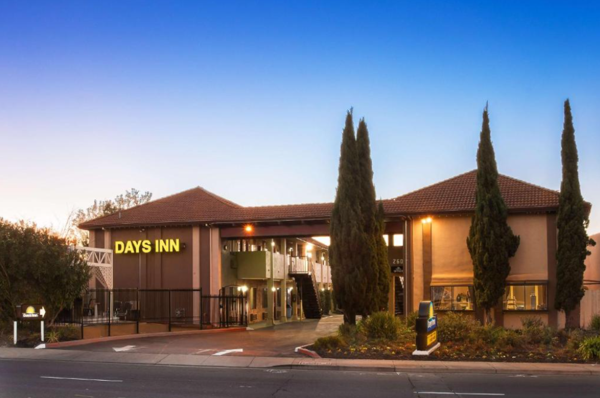 A Days Inn hotel building with a sign and surrounding trees, viewed in the early evening.