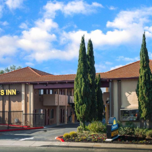 The image shows the exterior of a Days Inn hotel, with a red-tiled roof and some tall trees in front of it.