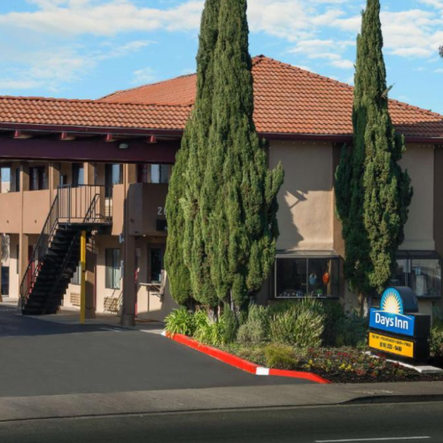 The image shows a hotel with a red-tiled roof, tall cypress trees, and a Days Inn sign by the entrance.