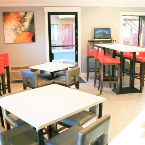 A modern cafe interior with white and red high chairs, a painting on the wall, and tables with chairs arranged neatly.