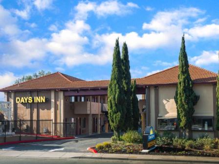 The image shows a Days Inn hotel building with a tiled roof, surrounded by trees and a clear sky.