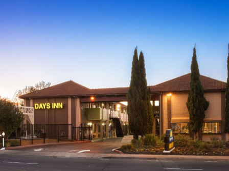 The image shows a Days Inn hotel with a brown roof, surrounded by trees and a clear sky at dusk.