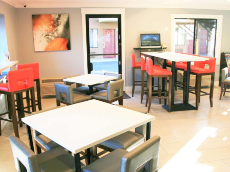 The image shows a modern cafe or lounge area with white tables, red and gray chairs, and a TV on the wall.