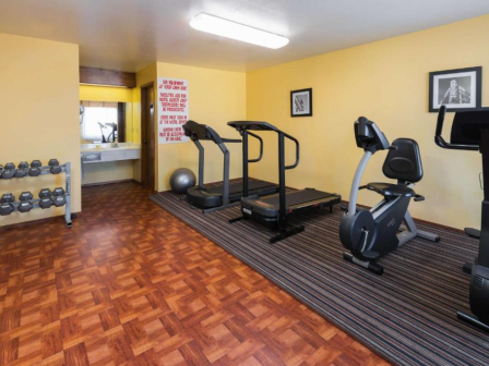 A small gym with treadmills, an exercise bike, weights, and a yoga ball, featuring a sink and motivational poster on a yellow wall.