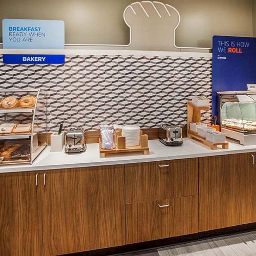 A breakfast station with pastries, toasters, and serving utensils on a wooden counter, featuring a bread-themed decoration on the wall.