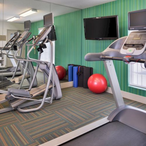 A gym with treadmills, elliptical machines, exercise balls, and wall-mounted TVs in a mirrored room.