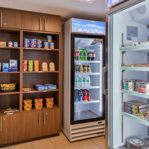 The image shows a snack area with shelves of snacks, instant noodles, and a fridge containing drinks, dairy, and other cold items.