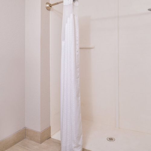 The image shows a minimalist shower area with a white curtain, handheld showerhead, and grab bar.