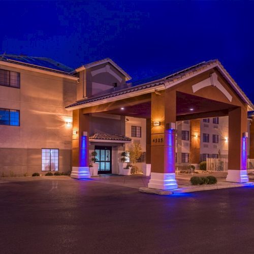 This image shows a hotel entrance at night with lights illuminating the exterior and an asphalt driveway leading up to the entrance.