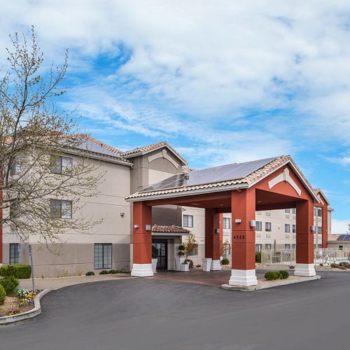 A hotel building with a red and white entrance, set against a partly cloudy sky, surrounded by trees and a paved driveway.