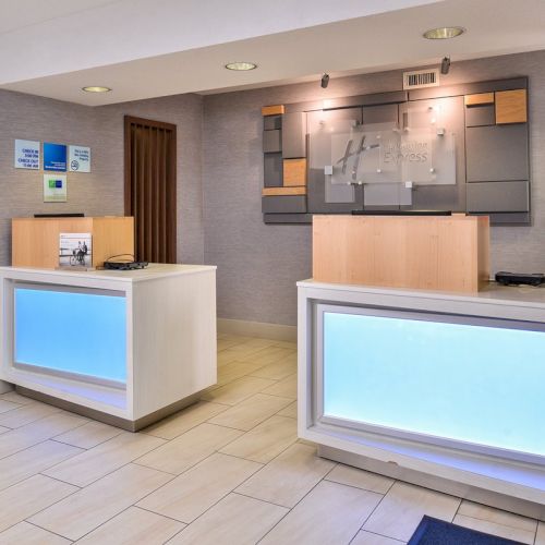 The image shows a hotel reception desk area with two counters, illuminated panels, and a modern décor style in a clean, bright environment.