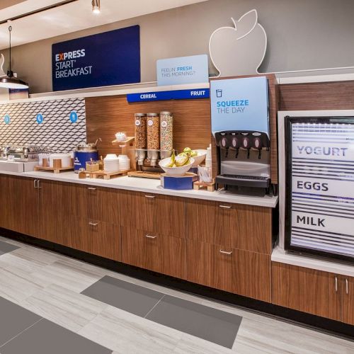 A breakfast buffet with cereal dispensers, yogurt, eggs, and milk fridge, and a juice section labeled 