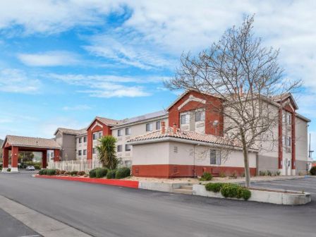 The image shows a two-story building, likely a motel or hotel, with a red and beige exterior, surrounded by a paved road and a few trees.