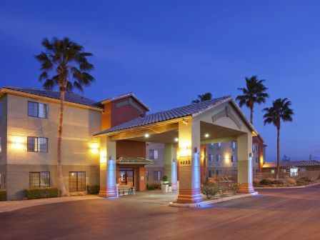 A hotel entrance at dusk with illuminated columns, palm trees, and a clear sky in the background.